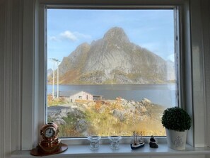 Una finestra con vista su una montagna, un piccolo edificio e una pianta in vaso.