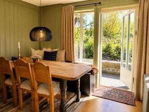 Un coin repas avec une table et des chaises en bois, un luminaire suspendu et une vue sur la verdure à travers une porte vitrée.