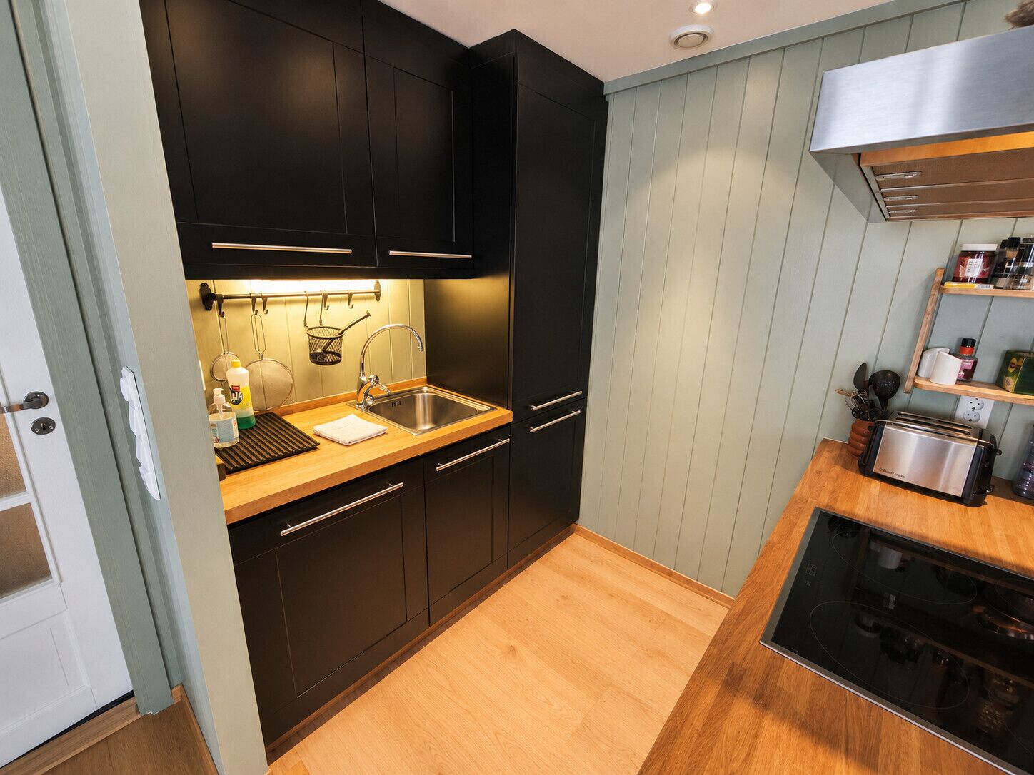 A compact kitchen with dark cabinets, a stainless steel sink, a toaster, and a built-in oven.