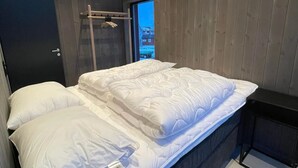 A modern bedroom with a wooden ceiling, a bed with white bedding, and a view of the outside through a window.