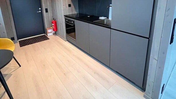 A modern kitchen with grey cabinets, a black countertop, and a wooden floor.