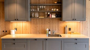 Une cuisine moderne avec des meubles gris, un plan de travail en bois et des étagères intégrées au-dessus de l’évier.