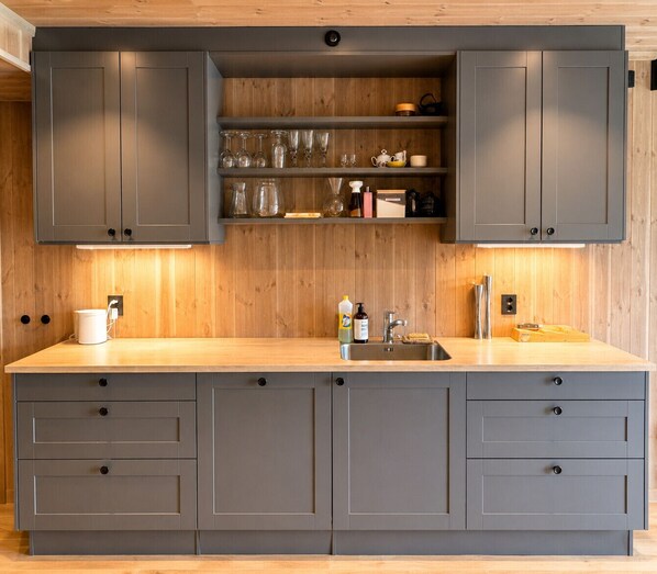 A modern kitchen with grey cabinets, a wooden countertop, and built-in shelves above the sink.