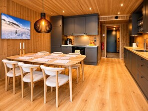 A modern kitchen with wooden cabinets, a dining area with a wooden table and chairs, and a hanging light fixture.