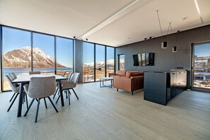 Un interior moderno con comedor, sofá y isla de cocina, ventanas amplias con vista a la montaña.