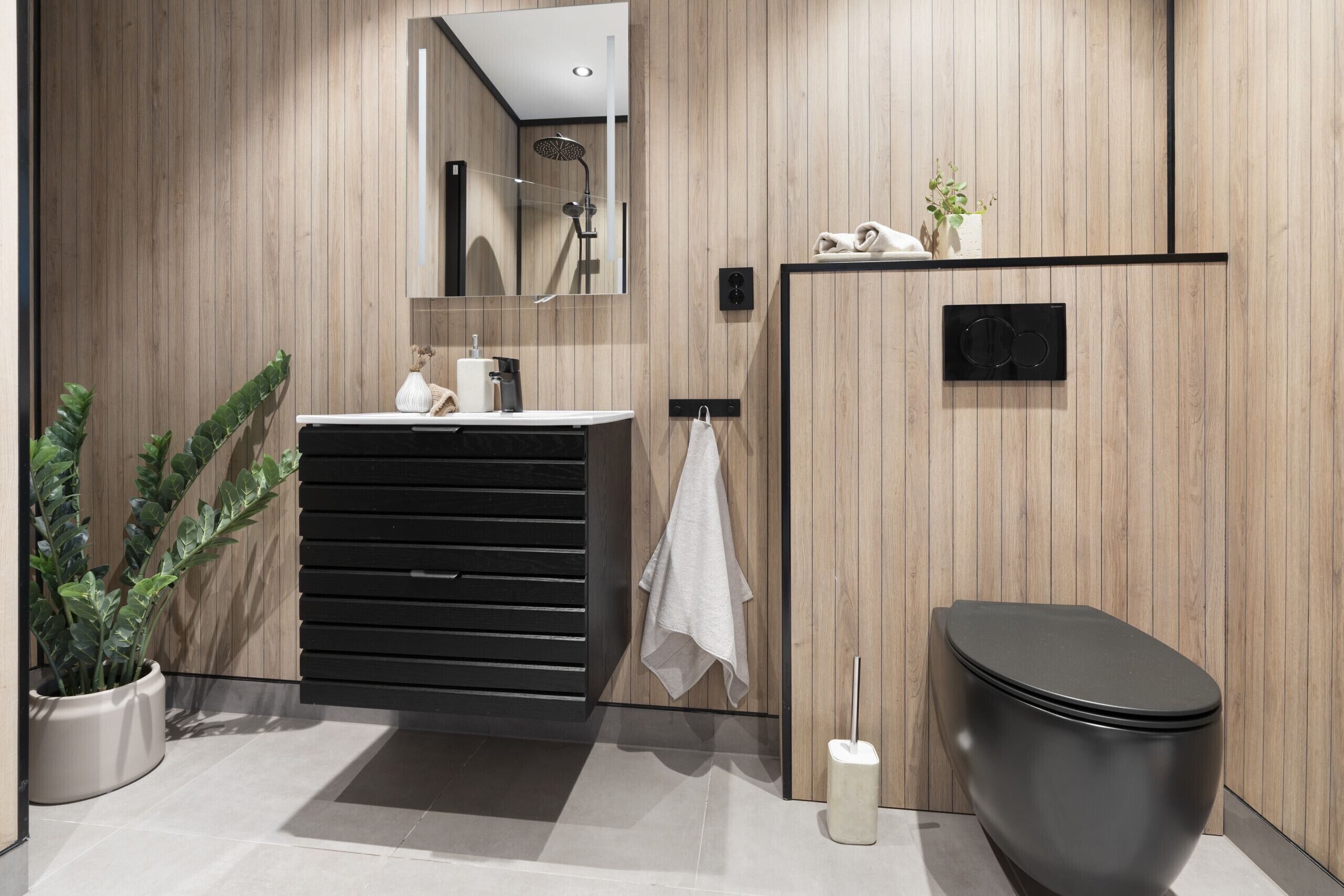 A modern bathroom with a wooden wall, a black toilet, a sink with a towel, and a mirror.