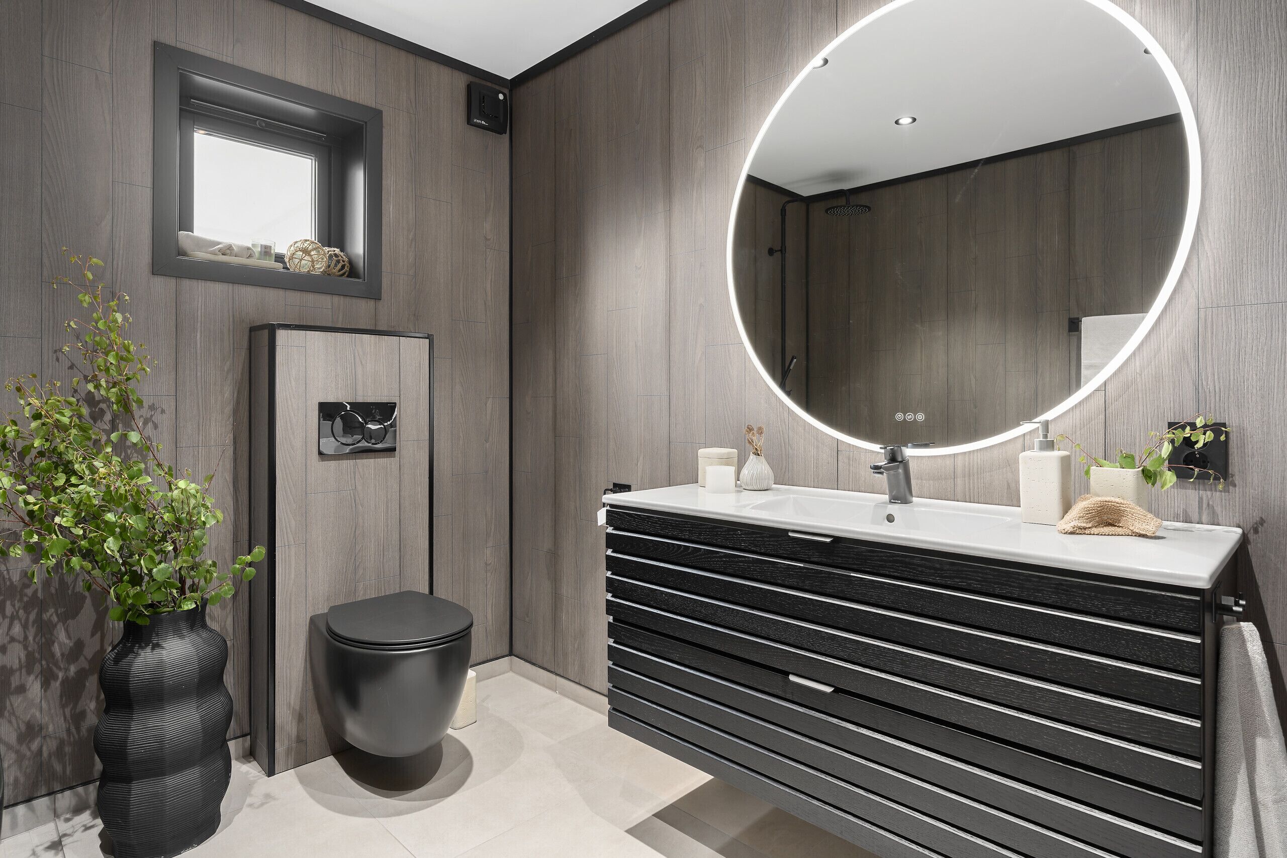 A modern bathroom with a large mirror, a toilet, a sink with a towel, and a potted plant.