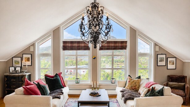 A loft-style room with a high ceiling, two sofas with throw pillows, a coffee table, a chandelier, and large windows with a view of greenery. - Sjelefred - stor leilighet med sentral beliggenhet (Hol)