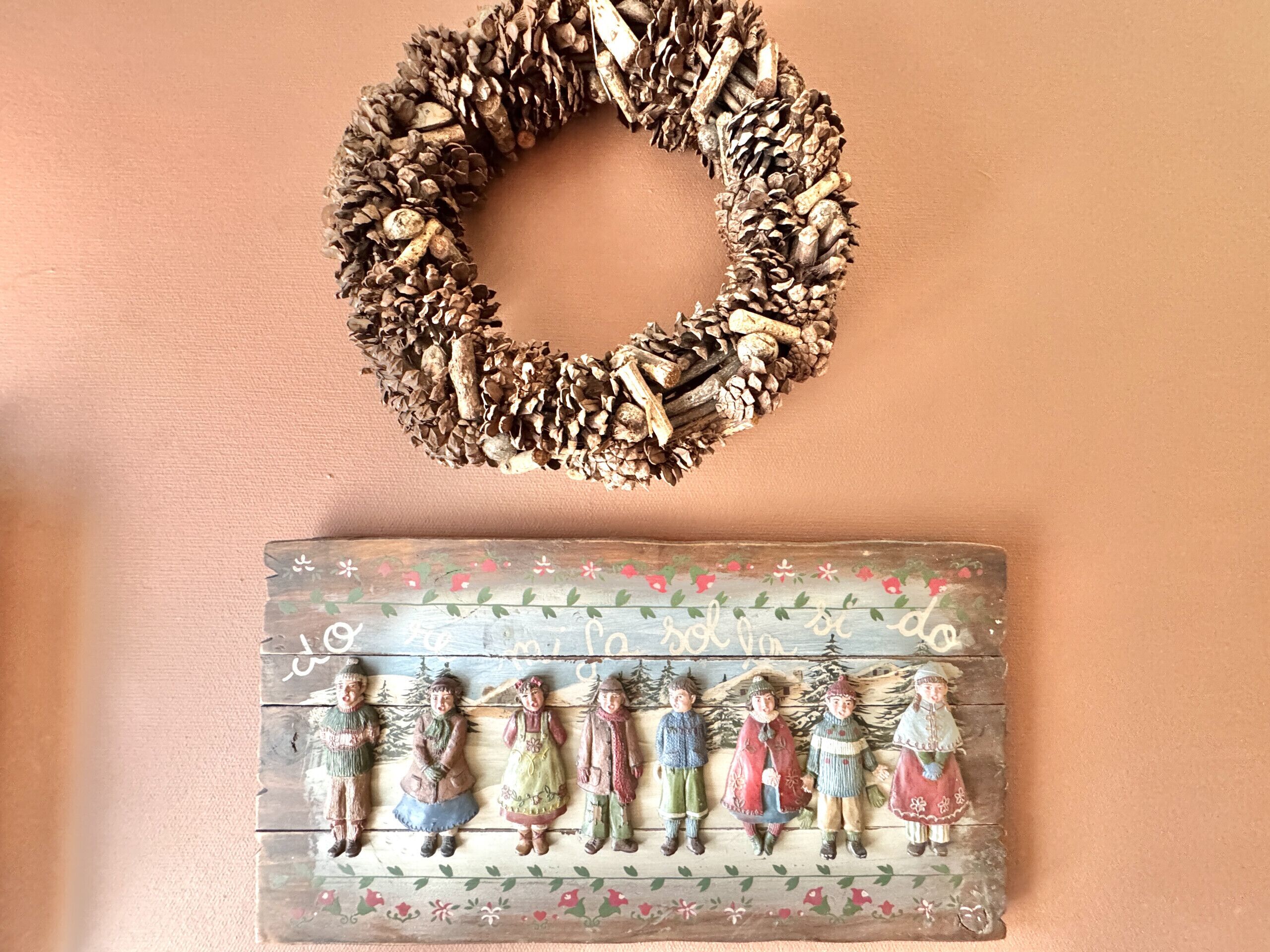 A pine cone wreath and a decorative plaque with figures.