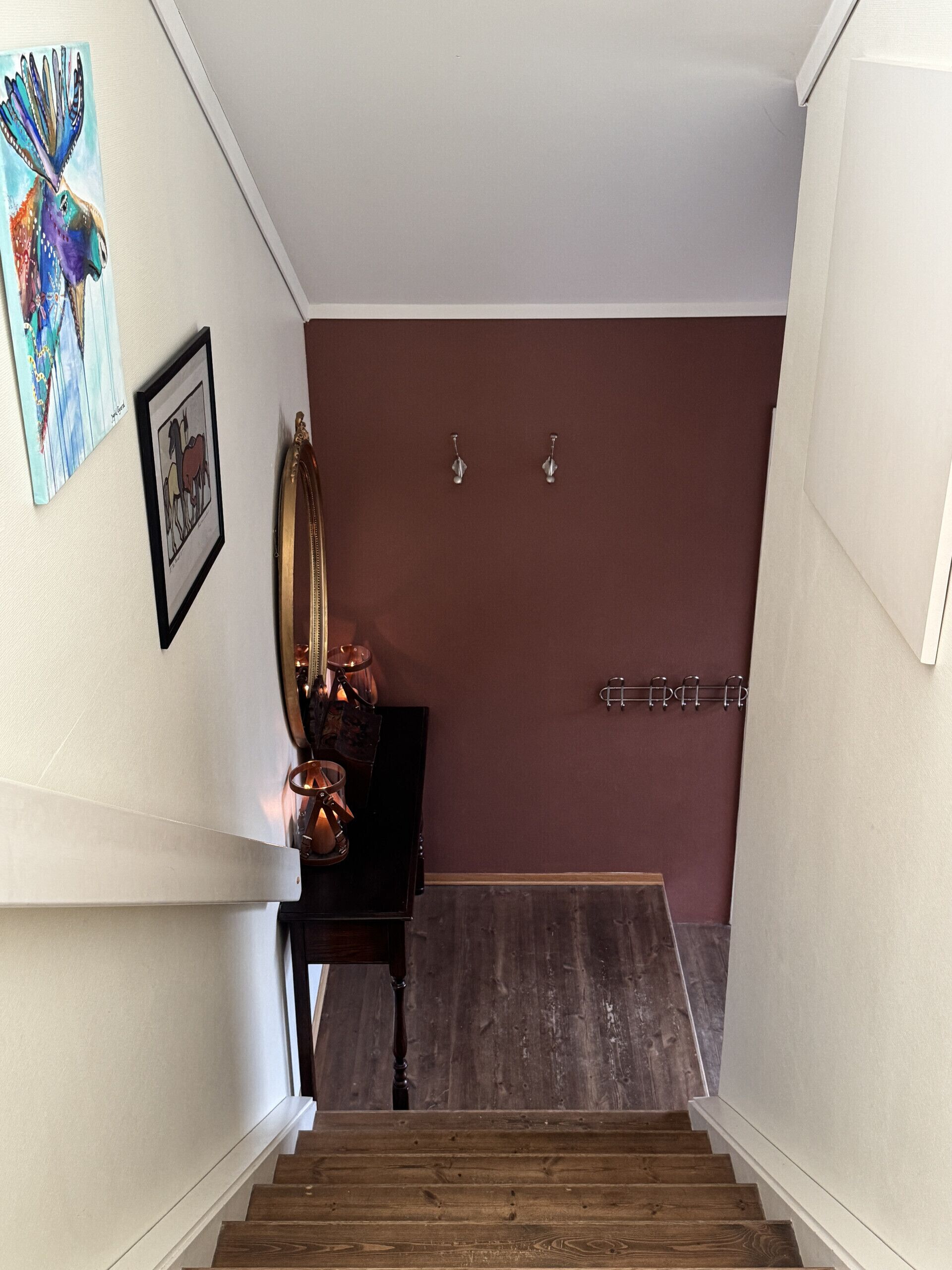 Una escala que condueix a una habitació amb terra de fusta fosca, una paret amb un quadre encapçalat i un llum fixada a la paret.
