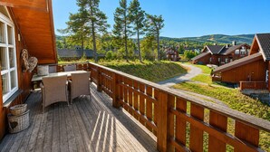 En träveranda med ett bord och stolar, med utsikt över en by med hus och träd.