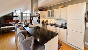 A modern kitchen with a central island, white cabinetry, and a dining area with a sofa and chairs. - Sjelefred - stor leilighet med sentral beliggenhet (Hol)
