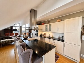 A modern kitchen with a central island, white cabinetry, and a dining area with a sofa and chairs. - Sjelefred - stor leilighet med sentral beliggenhet (Hol)