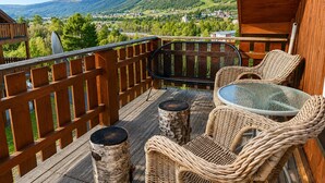 A wooden deck with wicker furniture, a glass table, and a view of a town and mountains. - Sjelefred - stor leilighet med sentral beliggenhet (Hol)