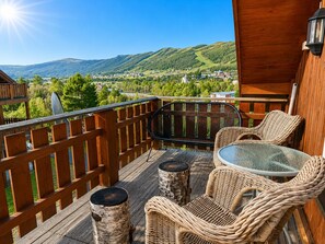 A wooden deck with wicker furniture, a glass table, and a view of a town and mountains. - Sjelefred - stor leilighet med sentral beliggenhet (Hol)