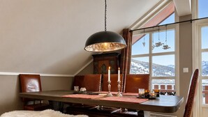 A dining area with a table, chairs, a fur throw, a chandelier, and a view of a snowy landscape through large windows. - Sjelefred - stor leilighet med sentral beliggenhet (Hol)