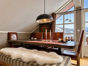 A dining area with a table, chairs, a fur throw, a chandelier, and a view of a snowy landscape through large windows. - Sjelefred - stor leilighet med sentral beliggenhet (Hol)