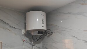 Egy márványfalas fürdőszoba, a falra szerelt fehér vízmelegítővel és egy jól látható elektromos konnektorral.