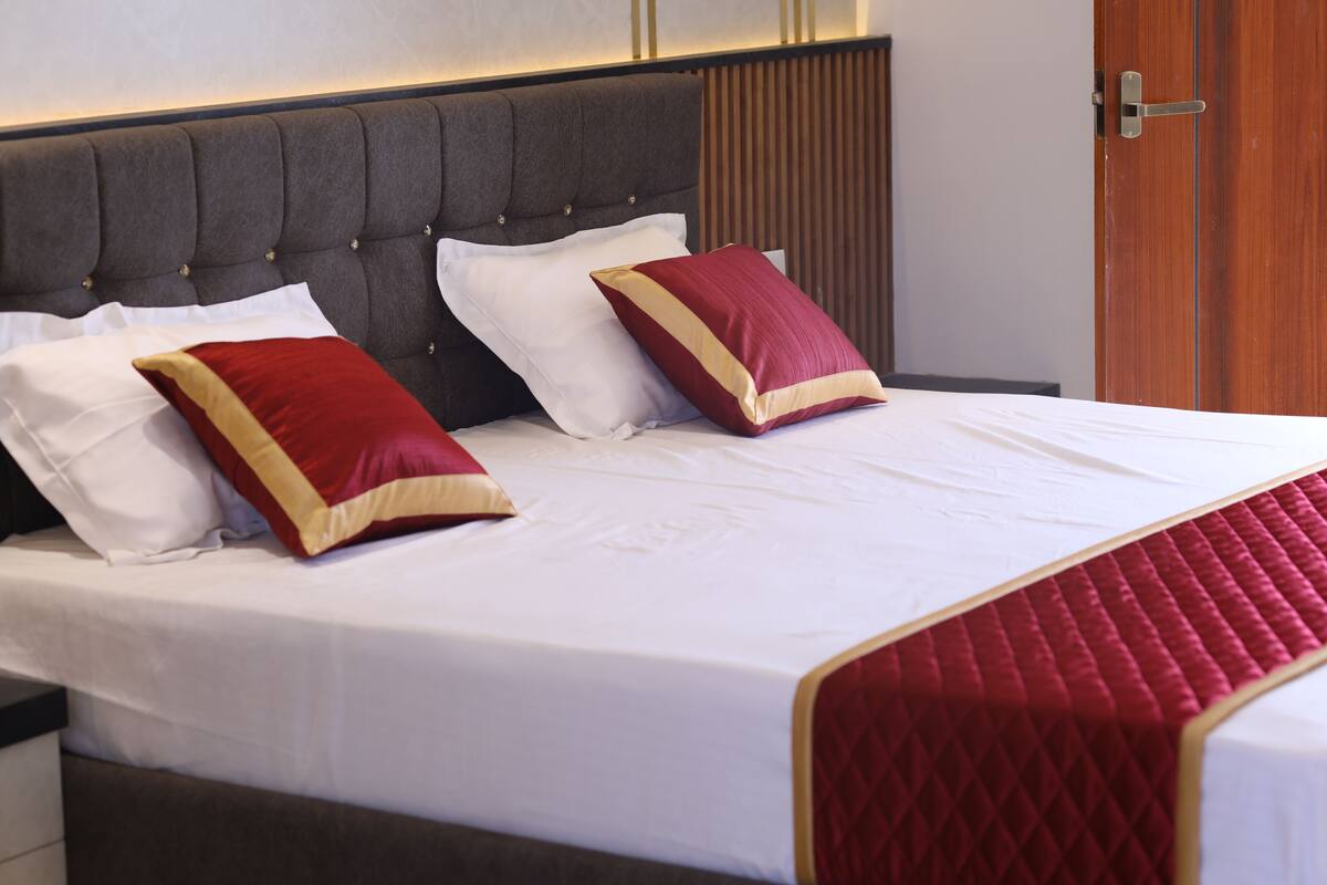 A neatly made bed with a quilted red and gold bedspread, a tufted headboard, and two pillows with a red and gold design.
