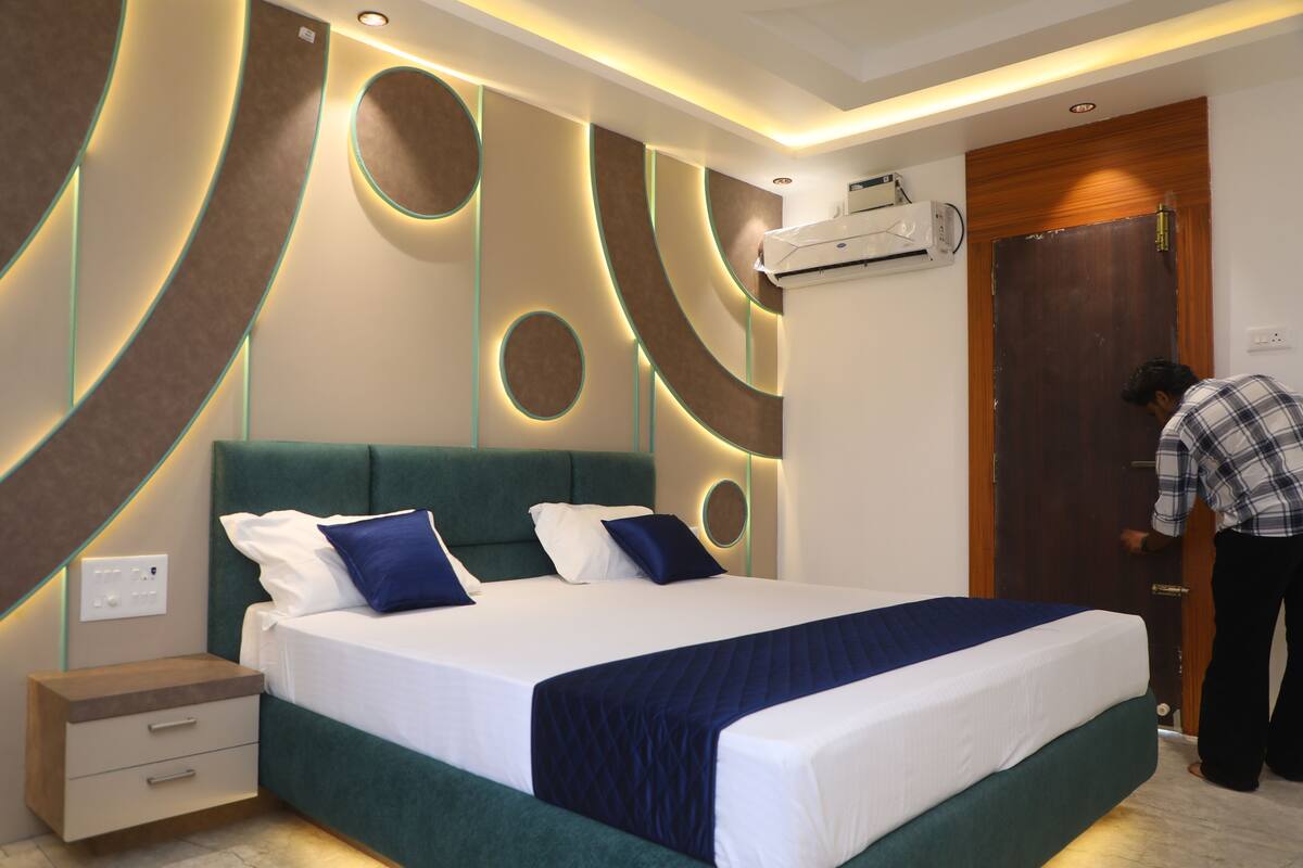 A modern hotel room with a large bed, a nightstand, a wall-mounted air conditioner, and a wooden door.