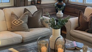 Una habitación acogedora con suelo de madera, un sofá color beige, una mesa con velas y vistas a un paisaje nevado a través de amplios ventanales.