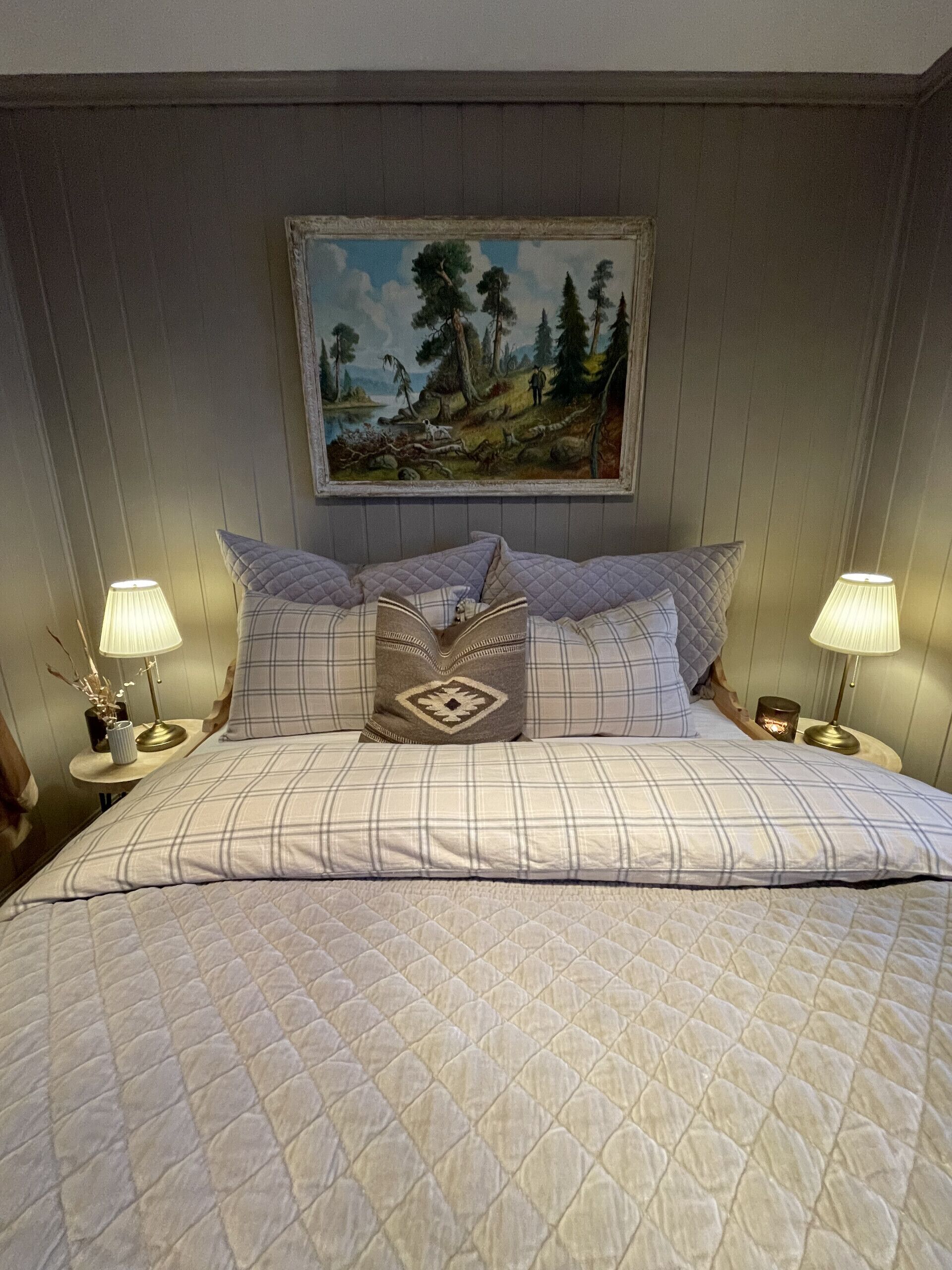 Ein Bett mit gesteppter Bettdecke, zwei Nachttischlampen, ein Gemälde an der Wand und ein kleiner Blumenstrauß auf dem Nachttisch.