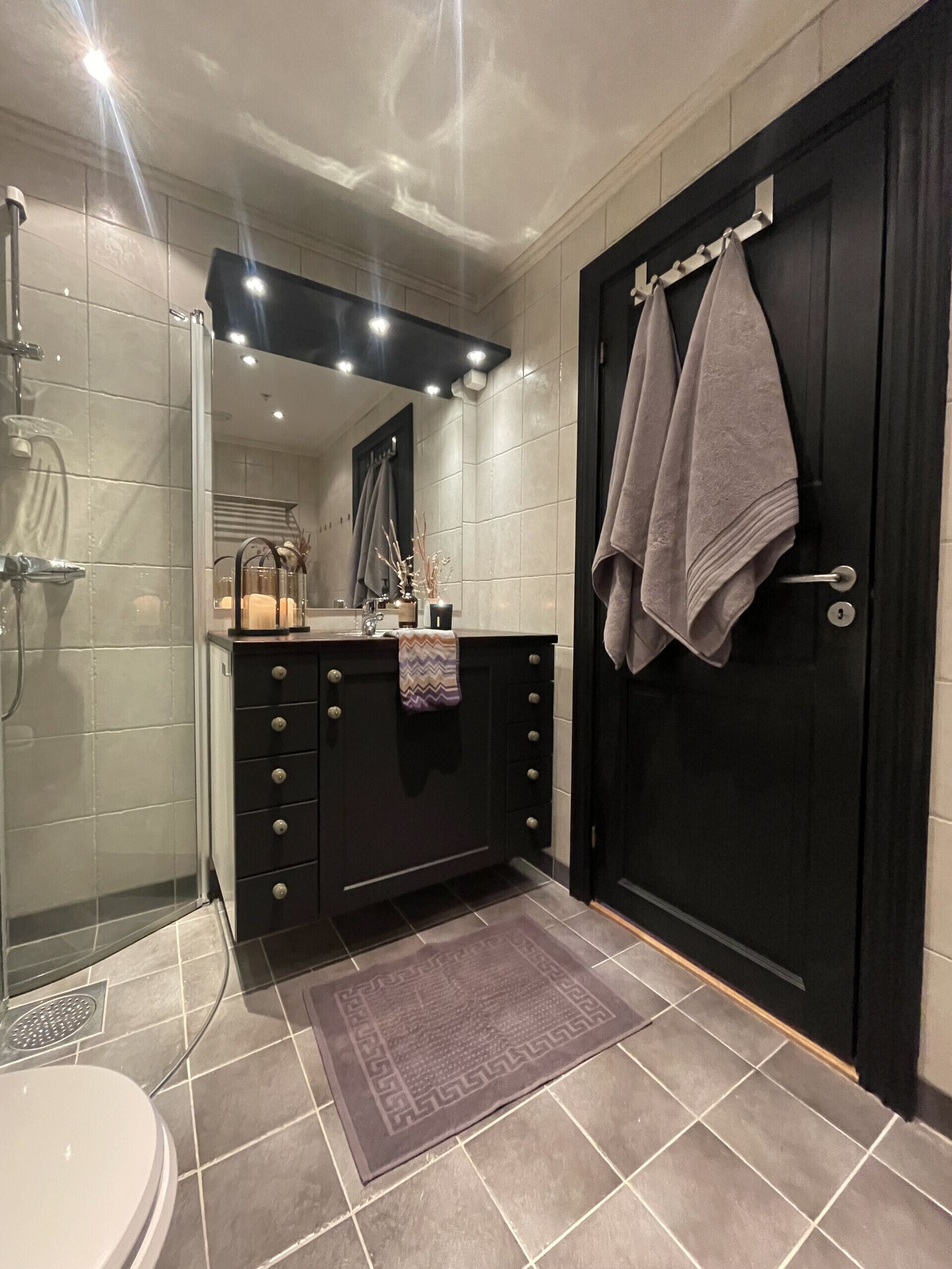 Un bagno moderno con cabina doccia in vetro, porta in legno scuro e pavimento piastrellato.