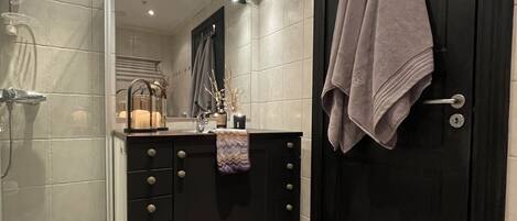 Un bagno moderno con cabina doccia in vetro, porta in legno scuro e pavimento piastrellato.