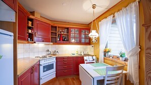 A kitchen with wooden cabinets, a white stove, a dining table with chairs, and a window with curtains.