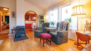 A cozy living room with a fireplace, comfortable seating, and a kitchen in the background.