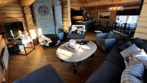 A log cabin interior with a stone fireplace, wooden ceiling beams, a television, and a cozy seating area. - Geilo centrum - cozy apartment - central location (Hol)
