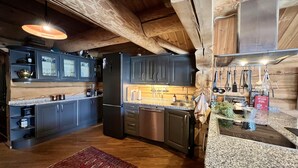 A kitchen with dark cabinets, stainless steel appliances, a wooden ceiling, and a red patterned rug. - Geilo centrum - cozy apartment - central location (Hol)