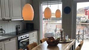 A modern kitchen with white cabinets, a wooden dining table, and pendant lights. - Amazing waterfront rorbu (free car-charging) (Vestvågøy)