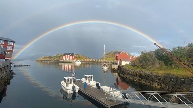 A harbor with boats docked, a rainbow, and buildings in the background. - Amazing waterfront rorbu (free car-charging) (Vestvågøy)