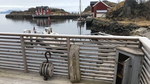 A wooden dock with a metal railing, a wooden post, and a small utility box. - Amazing waterfront rorbu (free car-charging) (Vestvågøy)