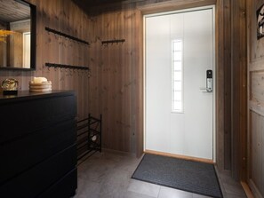 Un intérieur en bois avec une porte blanche, un banc noir et une petite table sur laquelle est posée une bougie.