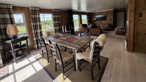 Ein Holzinterieur mit einem Esstisch, Stühlen, einer Couch und einem an der Wand befestigten Fernseher.