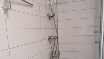 A bathroom with white tiled walls, a shower with a handheld showerhead, a handheld showerhead on the floor, and a metal towel rack.