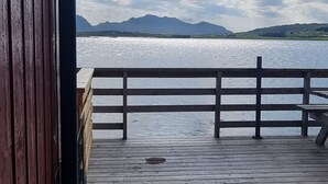 Une terrasse en bois dotée d’une rambarde, offrant une vue sur une étendue d’eau et sur des montagnes lointaines.