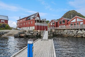 Una propiedad frente al agua con un muelle, edificios rojos y una colina rocosa al fondo.