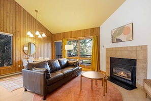 Ein gemütliches Wohnzimmer mit Ledersofa, Kamin und einem großen Fenster mit Vorhängen.