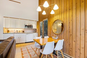 Eine moderne Küche mit weißen Schränken, einem Holztisch mit weißen Stühlen und einem runden Spiegel an der Wand.