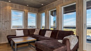 A room with a sectional sofa, a coffee table, and large windows offering a view of the outdoors.