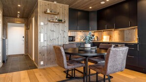 A modern kitchen with dark cabinets, a wooden ceiling, and a dining area with a round table and chairs.