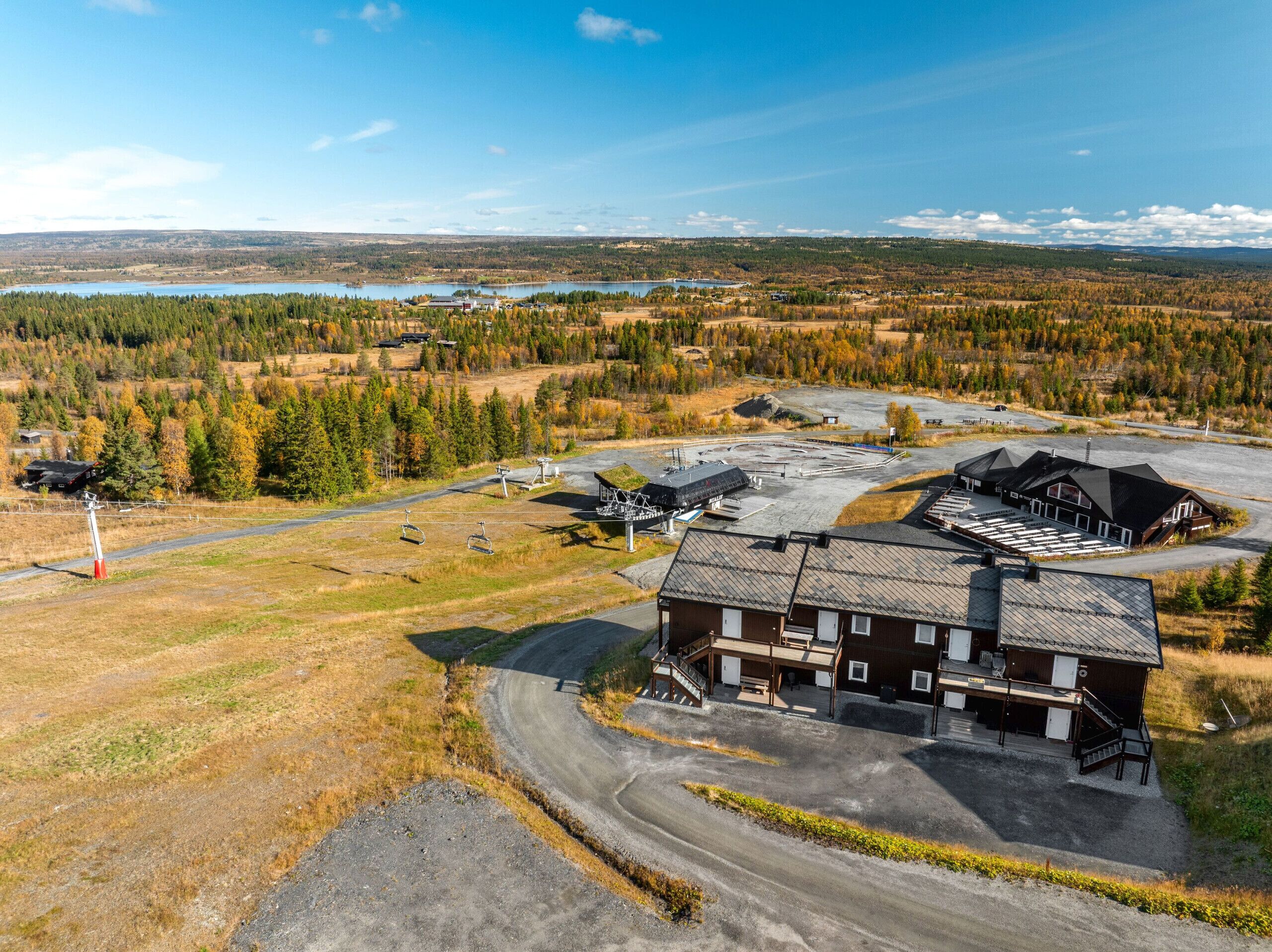 En stuga med en stor byggnad, en skidlift och utsikt över en sjö och en skog.