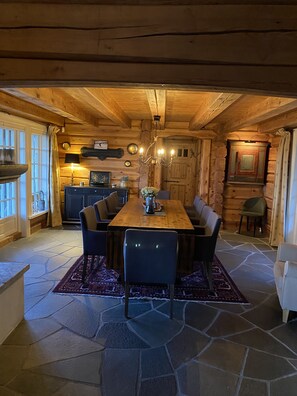 Un intérieur en bois comprenant une table à manger, des chaises, un lustre et un revêtement de sol en pierre.