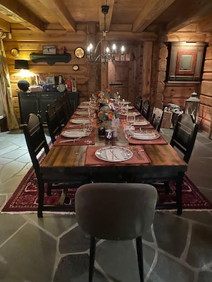 Ein Esszimmer aus Holz mit einem langen Tisch, der für eine Mahlzeit gedeckt ist, umgeben von Stühlen.