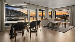 A modern living room with a dining area, large windows with a mountain view, and a cozy seating arrangement. - Premium Waterfront Apartment–Sea & Mountain View (Tromsø)