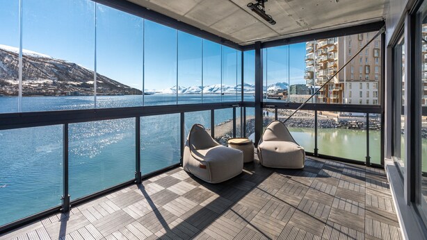 A balcony with a view of a body of water and mountains, furnished with two bean bags and a small table. - Premium Waterfront Apartment–Sea & Mountain View (Tromsø)