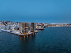 Ein Hotel am Wasserufer, mit moderner Architektur, einem Steg und Blick auf die Skyline der Stadt.